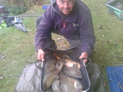 Photo of man at the lakeside holding a basket full of caught carp