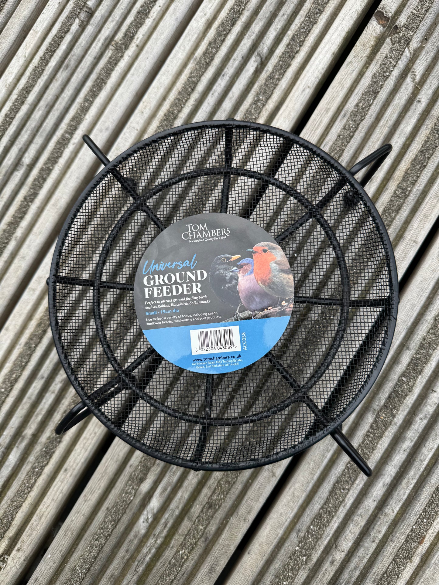 Black metal ground feeder with a label on a wooden surface