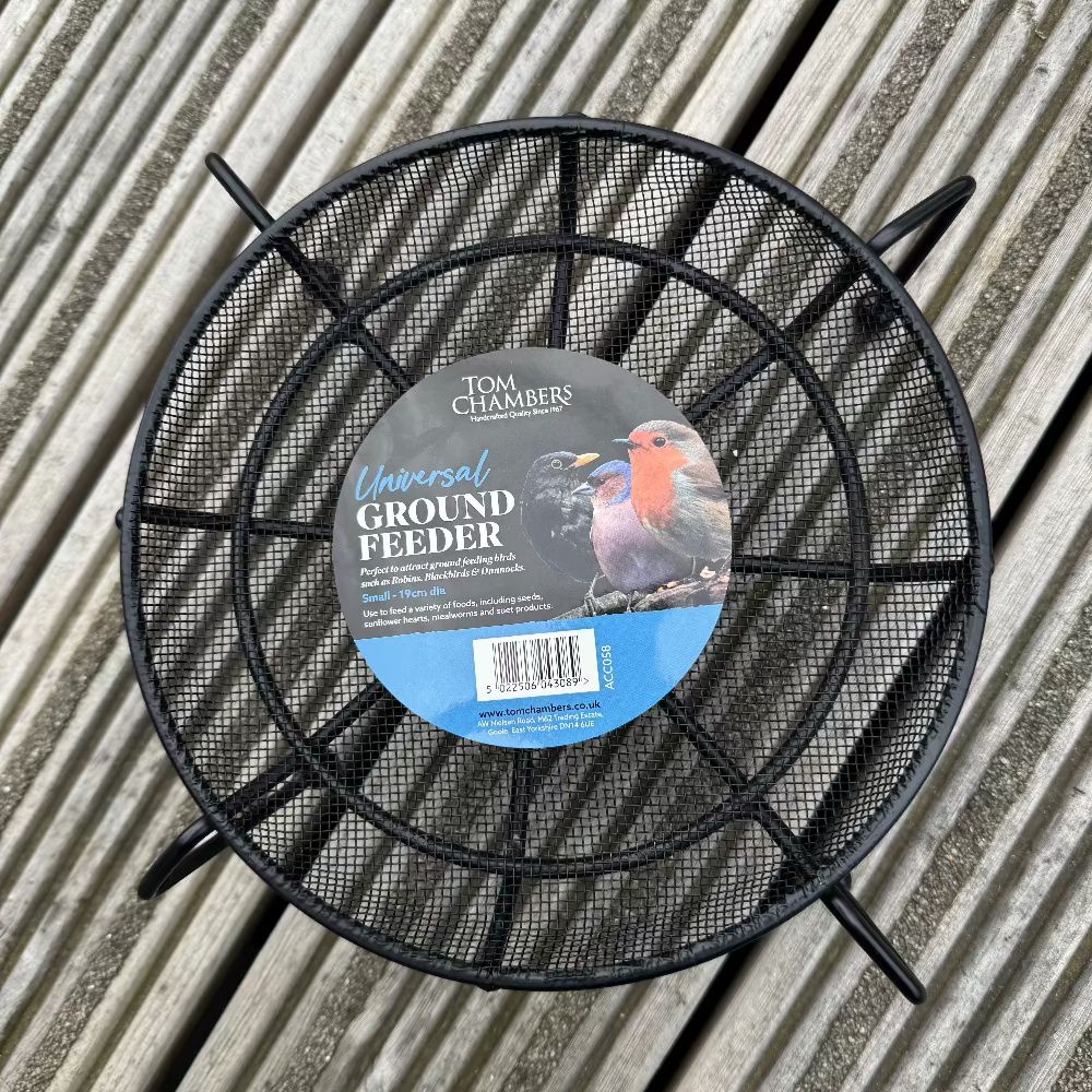 Black metal ground feeder with a label on a wooden surface