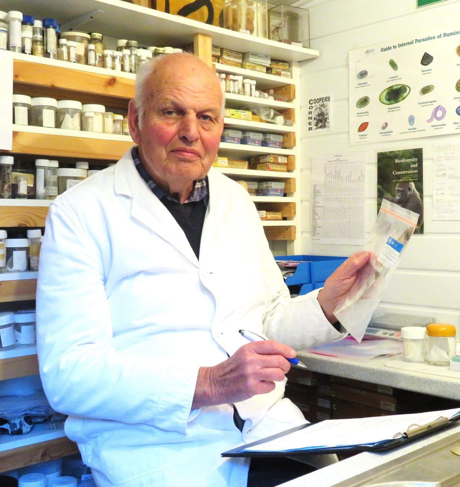 John E Cooper in a lab coat, sat at a desk.