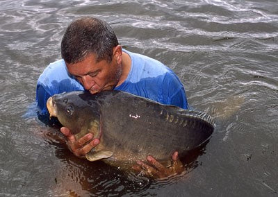 Image of Ken Townley stood in a lake kissing a large carp