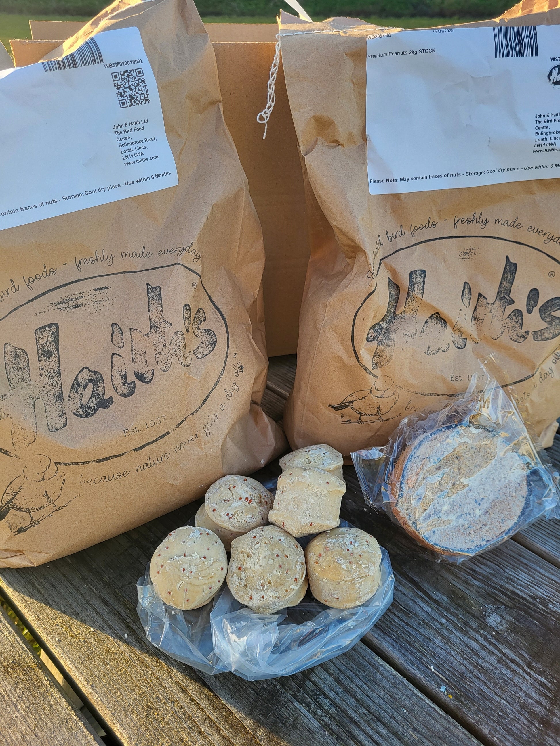 two bags of seed, a coco fat feeder & 6 suet balls on a wooden bench