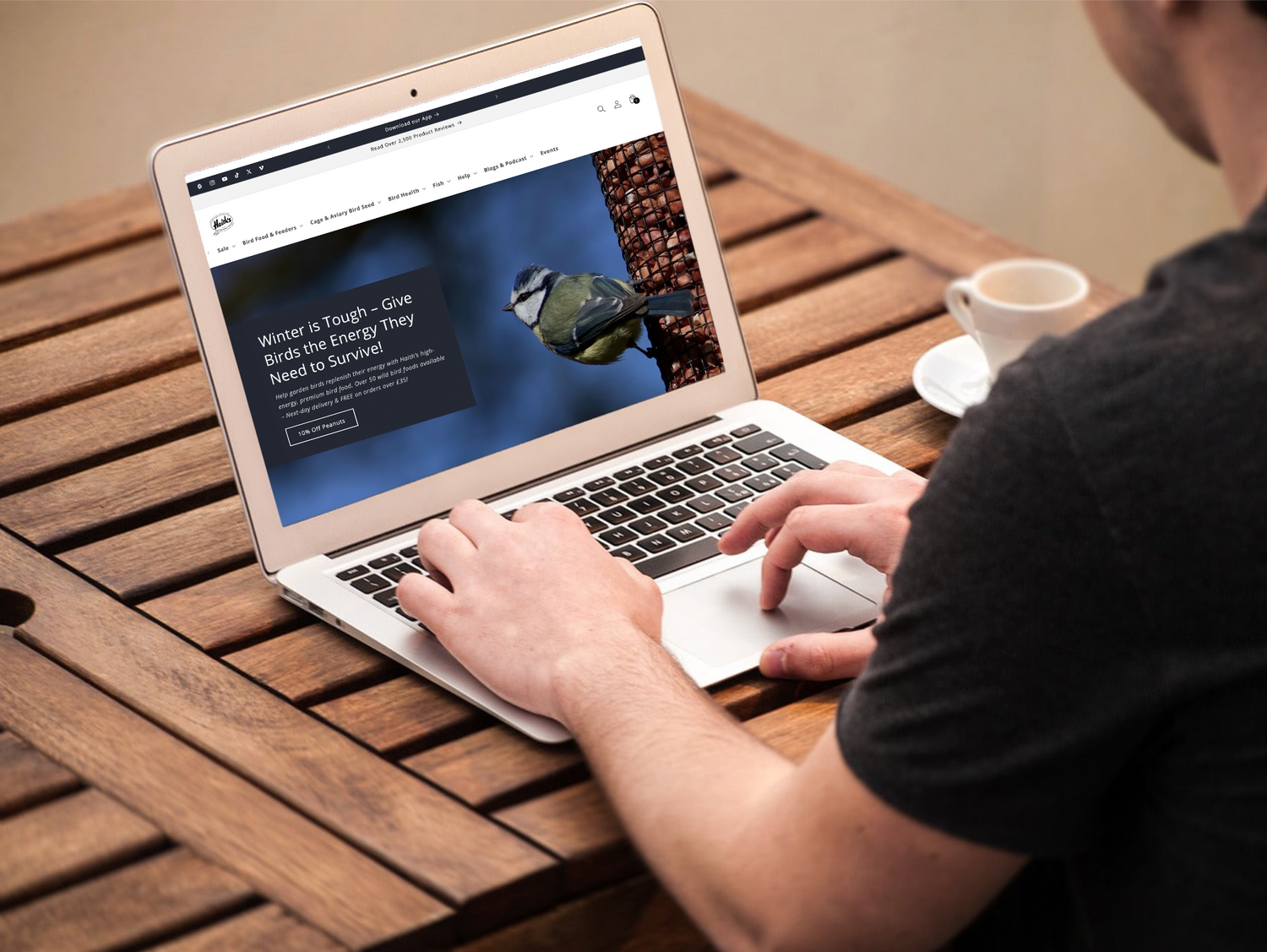 man using a laptop computer sat at a wooden table 