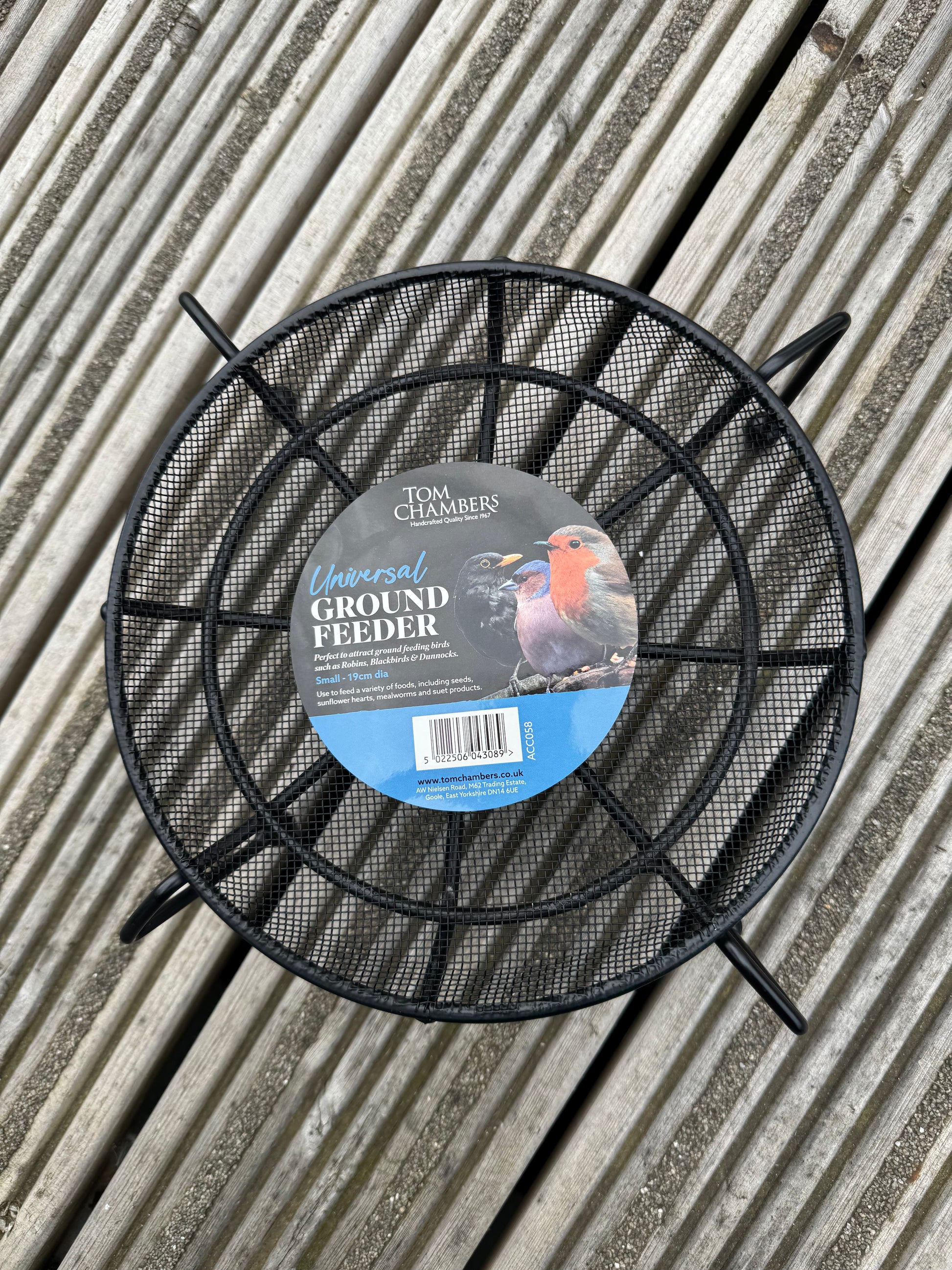 Black metal ground feeder with a label on a wooden surface