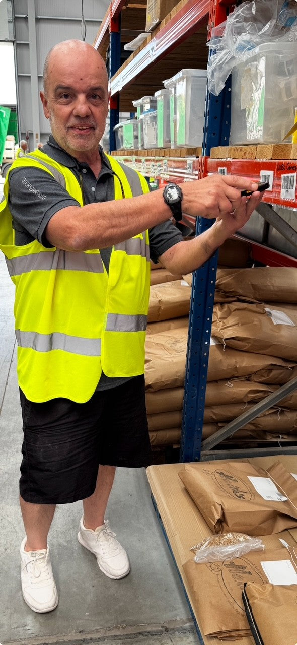Man in a warehouse wearing a yellow safety vest using a handheld device.