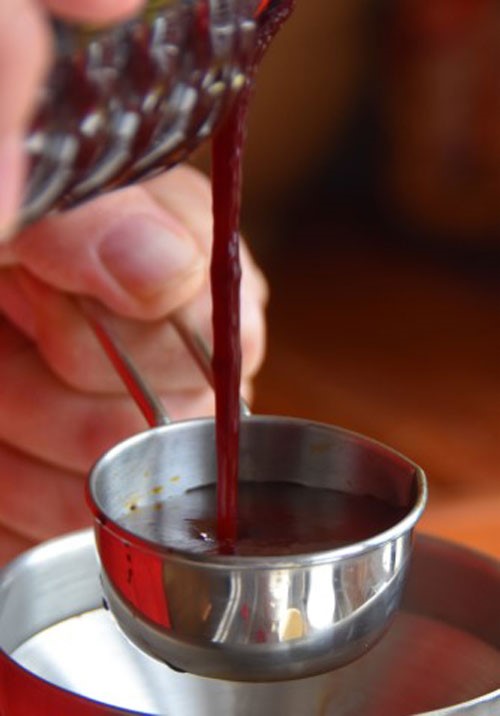 hand pouring out a red liquid into a steel cup
