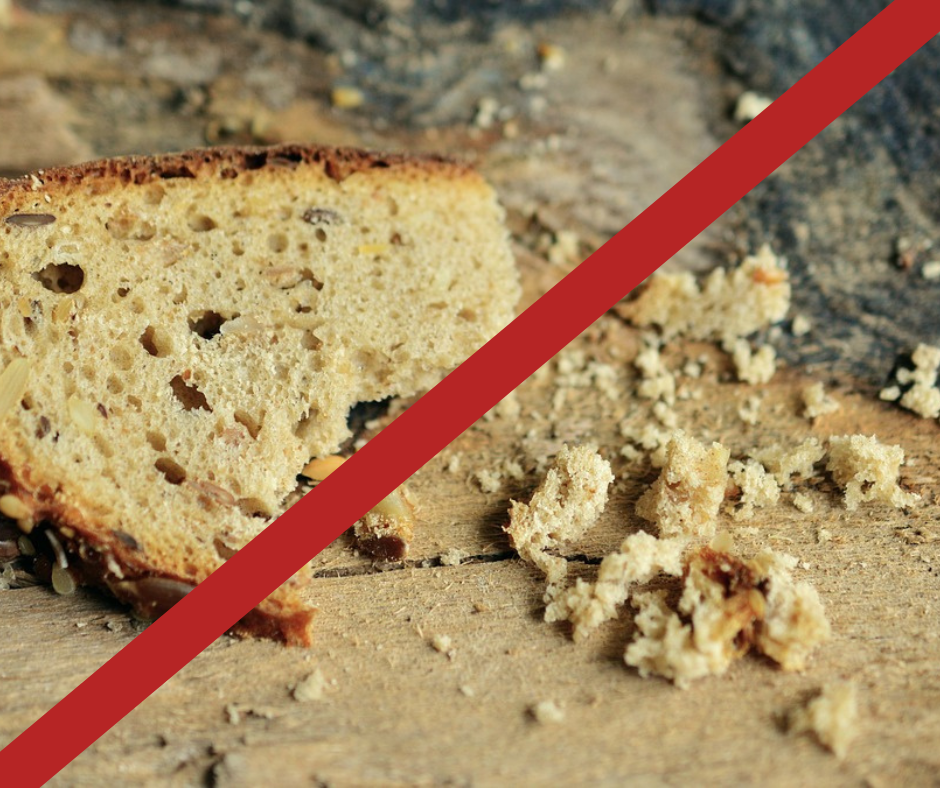 Sliced bread with crumbs on a wooden surface, crossed out with a red line.