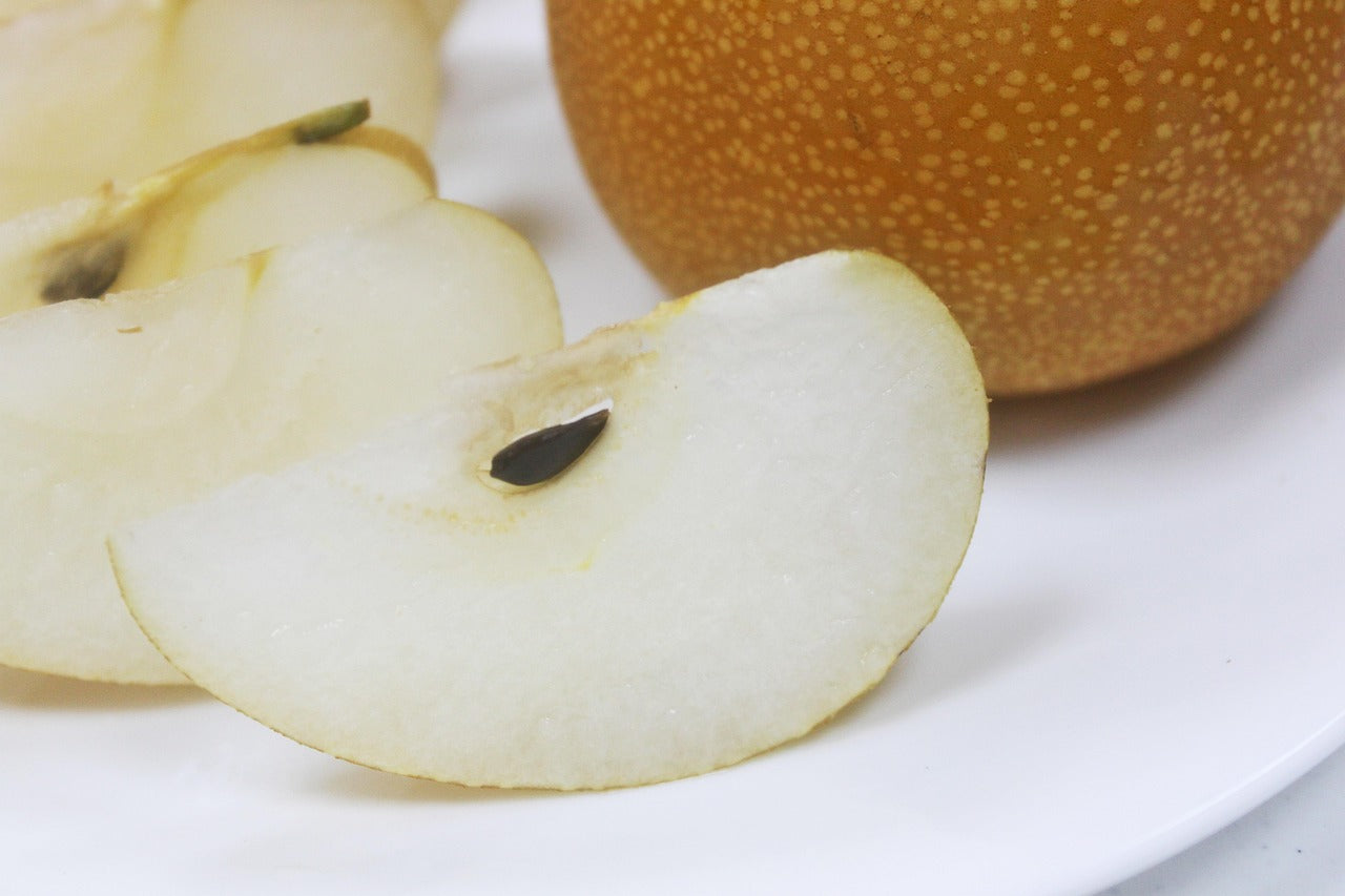 Sliced pear on a white plate with a whole pear in the background