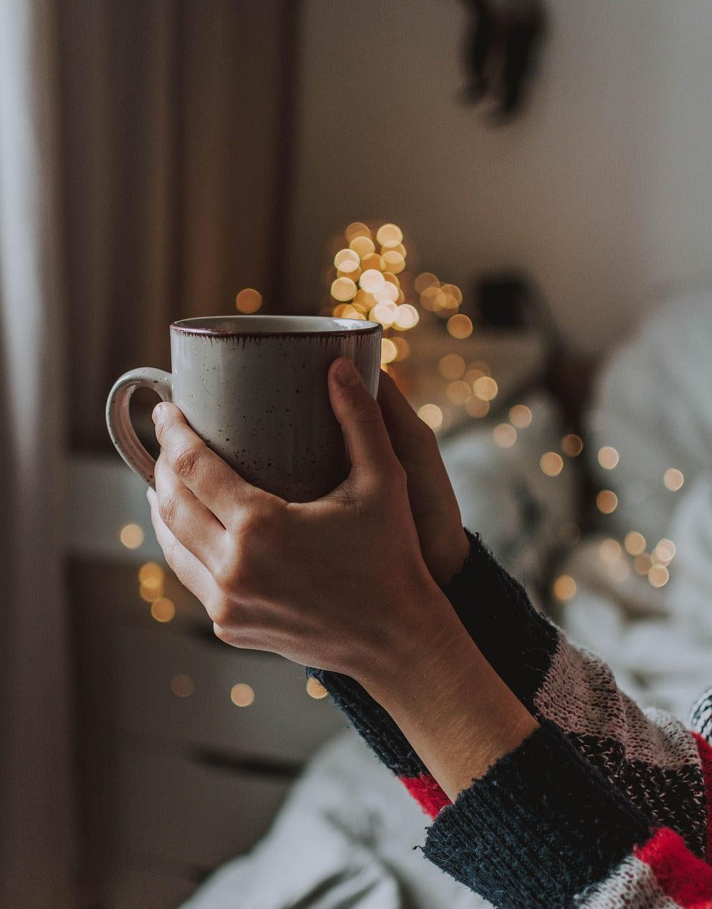 hand holding a coffee with twinkly background lights