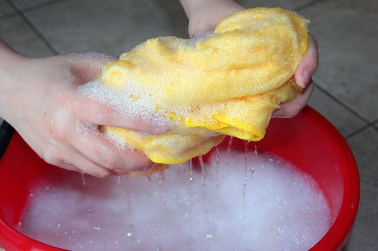 a yellow rag being wrung out over a red bucket full of soapy water