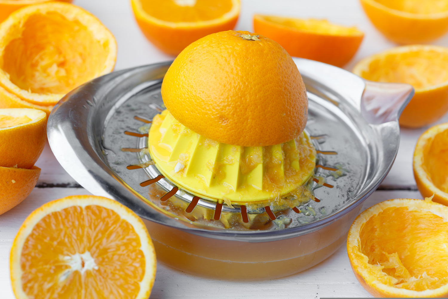 Orange being juiced with a manual juicer surrounded by halved oranges on a white background